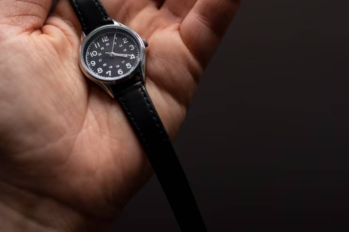  A close-up of a silver analog watch with a black face, resting in a person's hand against a dark background. 