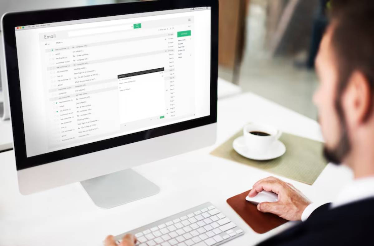 A person uses a computer mouse while viewing an email interface on a screen, with a cup of coffee nearby.