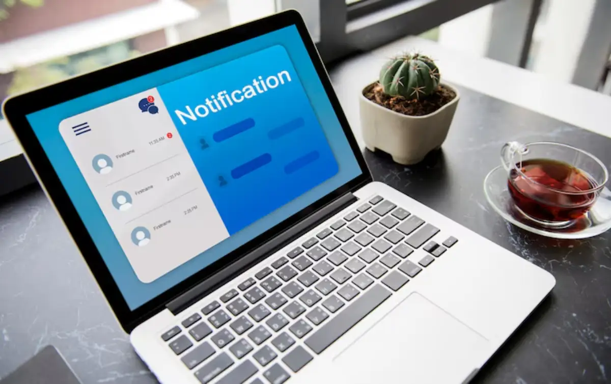 A laptop displaying a notification interface, with a cactus plant and a cup of tea beside it on a marble tabletop. 