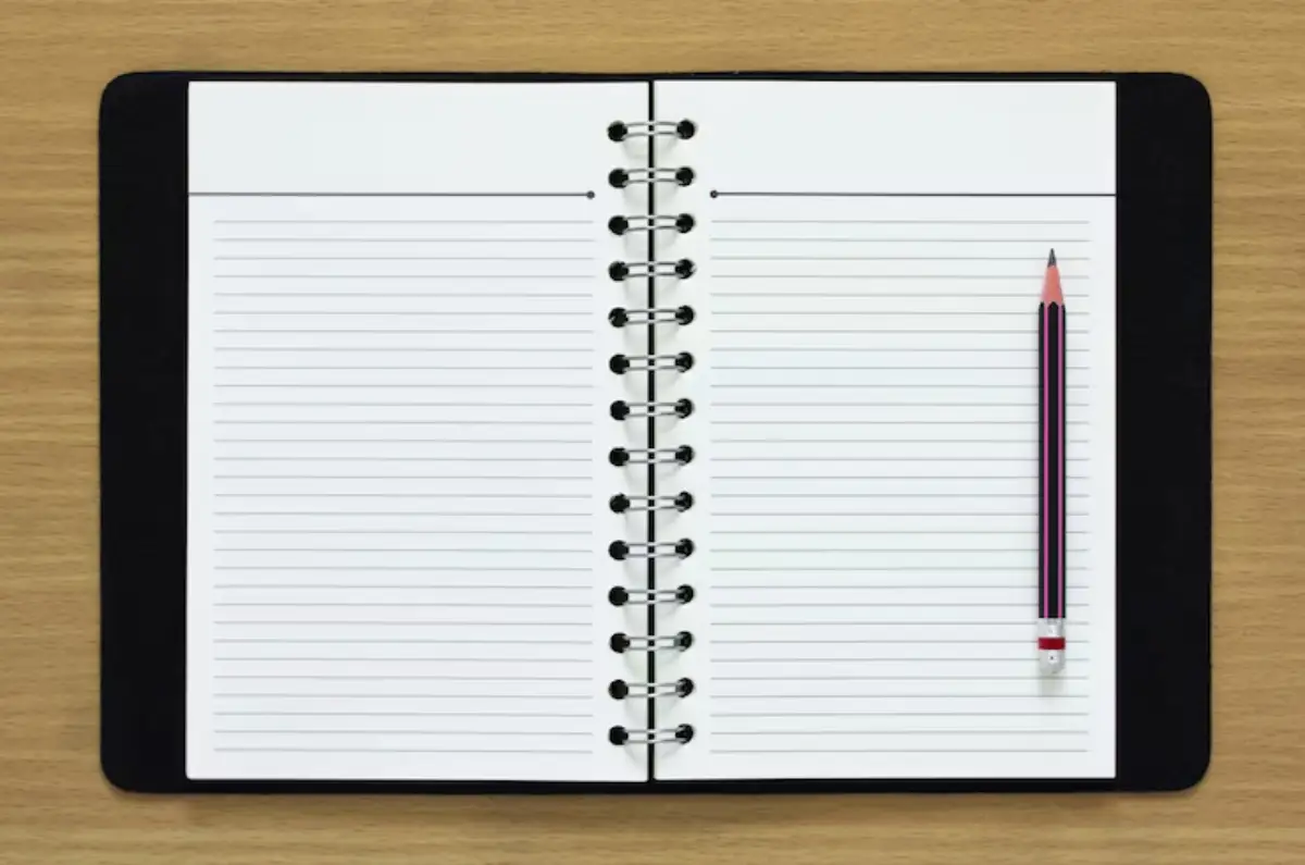  Open notebook with blank lined pages and a pink-striped pencil resting on the right side, set on a wooden table.