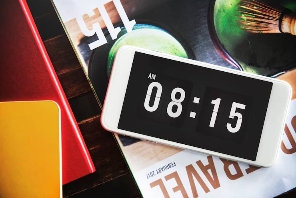 A smartphone displaying the time 08:15 AM, placed on a stack of colorful notebooks and a magazine featuring green food items.
