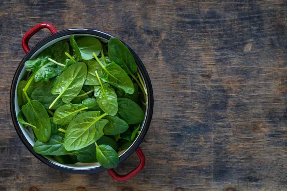 A bowl filled with fresh green spinach leaves sits on a rustic wooden surface, showcasing the vibrant foliage.