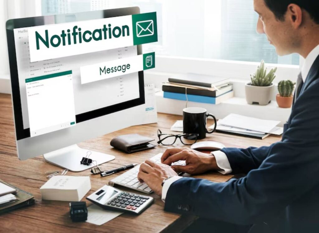 A person in a suit types on a keyboard, with a desktop displaying email notifications and a tidy office workspace.