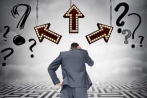 A man in a suit stands confused, facing three lit directional arrows surrounded by question marks, symbolizing decision-making.