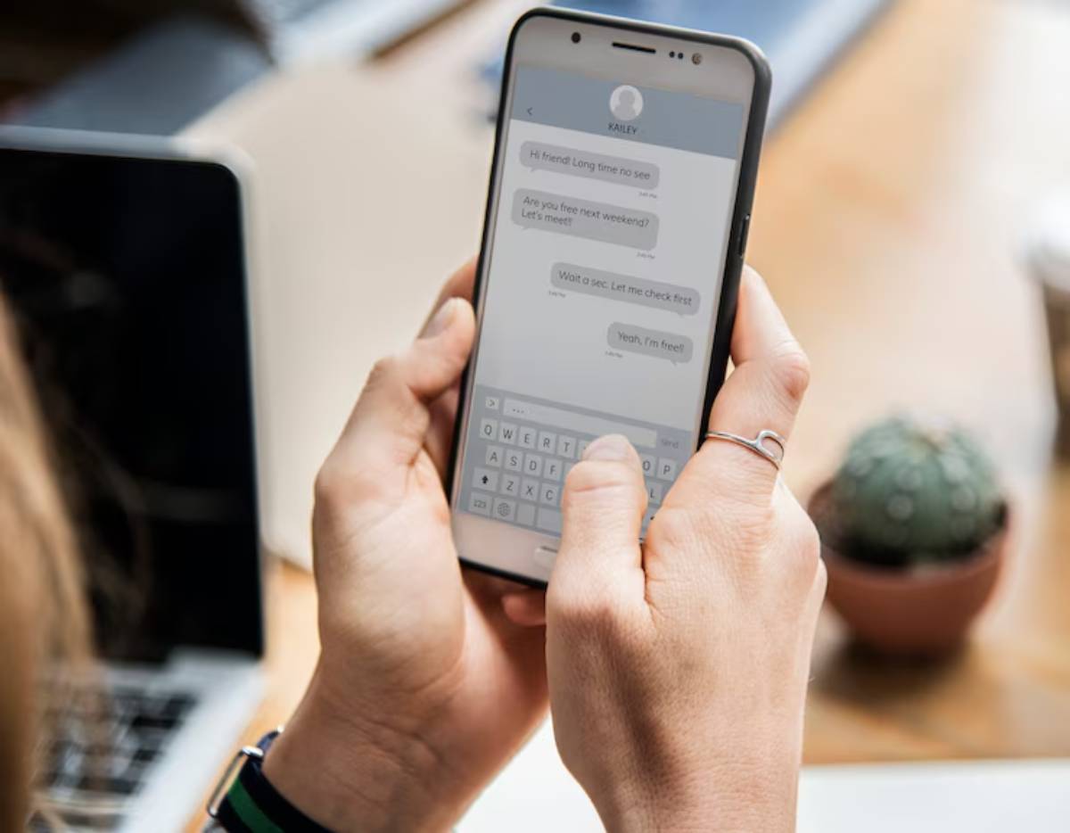 A person is texting on a smartphone about meeting up with a friend, with a cactus visible in the background.