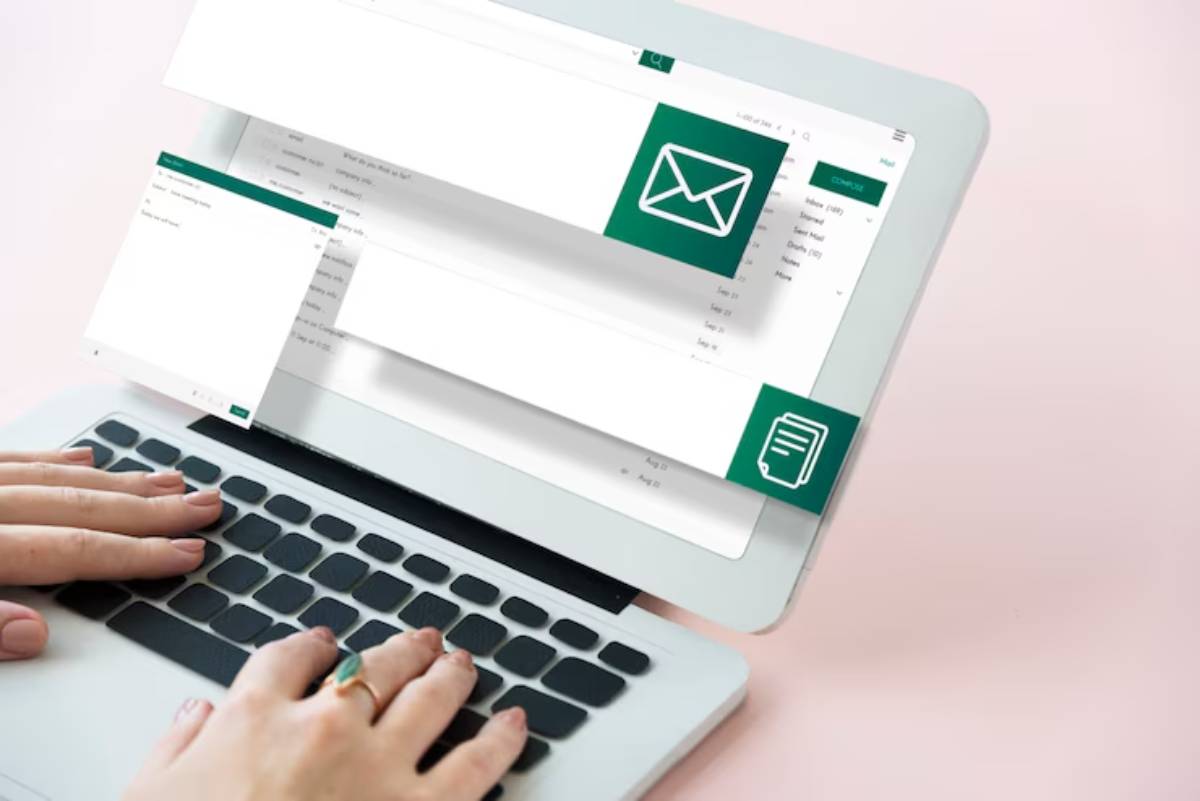 A person types on a laptop keyboard with email and document icons displayed on the screen, set against a soft pink background.