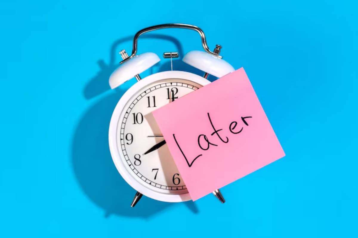 A white alarm clock with a pink sticky note reading Later on its face, set against a bright blue background.